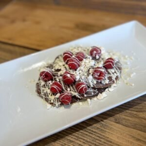 3 fluffy protein pancakes drizzled with white chocolate, topped with crushed meringue, and finished with fresh raspberries.