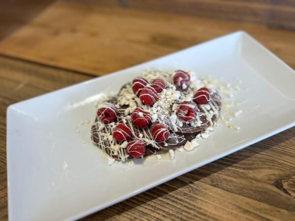 3 fluffy protein pancakes drizzled with white chocolate, topped with crushed meringue, and finished with fresh raspberries.