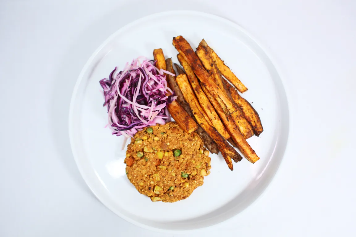 A plant-based burger served with roasted sweet potato wedges and a side of fresh slaw.