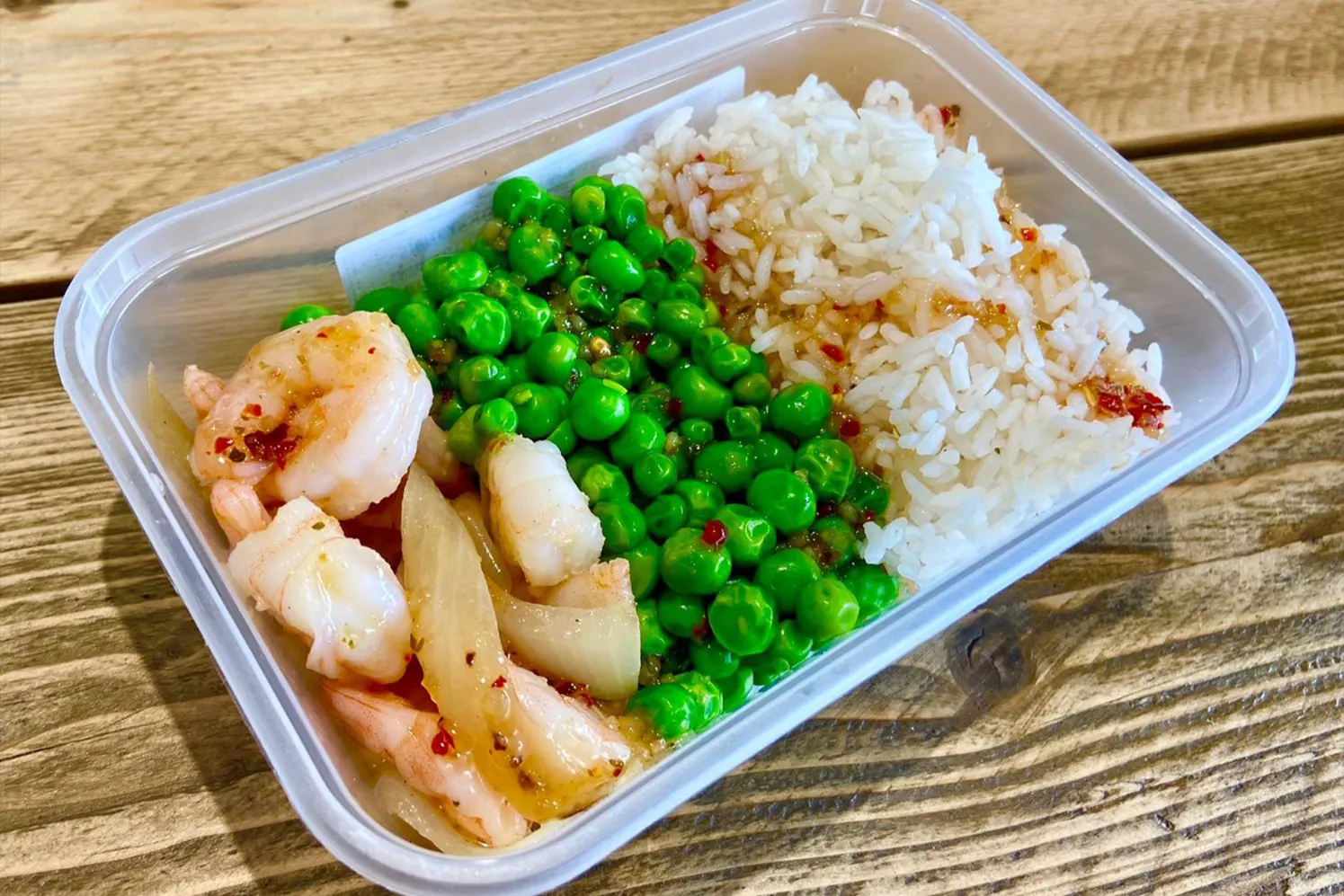 Sticky Thai King Prawn dish served over white rice with sweet peas and caramelized onions, drizzled with a spicy Thai sauce for a perfect blend of flavor and nutrition.