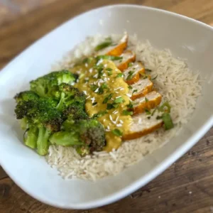 A bowl of Thai Green Curry with chicken, served over jasmine rice, and a sode of broccoli.