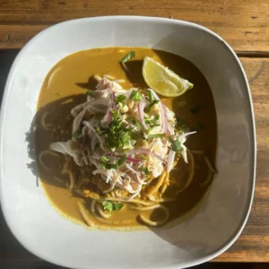 A bowl of Thai Noodle Soup. Tender noodles swim in a fragrant, coconut-infused curry broth, spiced to perfection, with a choice of lean chicken or crispy tofu to make this a satisfying, hearty meal. Topped off with a squeeze of lime and sliced red onion.