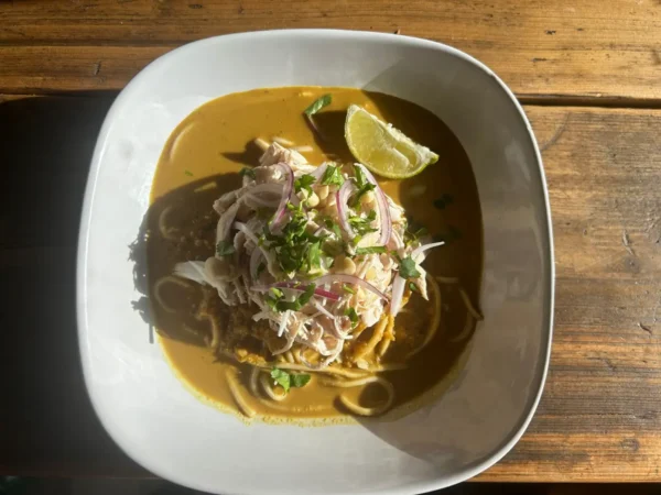 A bowl of Thai Inspired Ramen Noodles. Tender noodles swim in a fragrant, coconut-infused curry broth, spiced to perfection, with a choice of lean chicken or crispy tofu to make this a satisfying, hearty meal. Topped off with a squeeze of lime and sliced red onion.