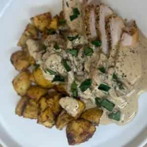 Double Parmesan Chicken with creamy mushroom sauce and roast potatoes on a white plate by Savage Kitchen