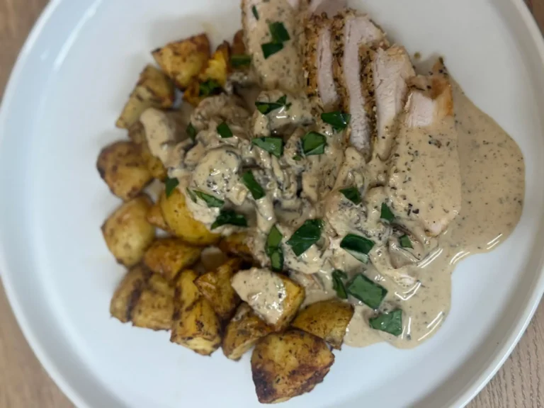 Double Parmesan Chicken with creamy mushroom sauce and roast potatoes on a white plate by Savage Kitchen