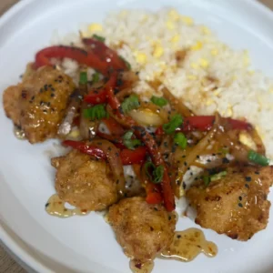 Crispy honey-glazed chicken bites served with egg-fried rice, sautéed red peppers and onions, topped with spring onions and black sesame seeds on a white plate, by Savage Kitchen