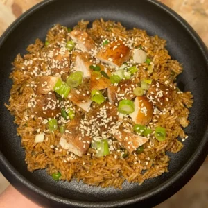 Fragrant Sesame Honey Fried Rice with chicken, edamame, peas, and spring onions. High protein, balanced, and full of sweet-savory flavour, presented on a black plate.
