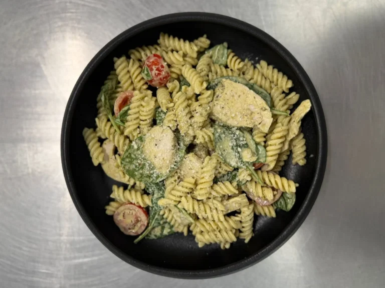 Pesto Pasta with cherry tomatoes, spinach and grated parmesan in a black bowl