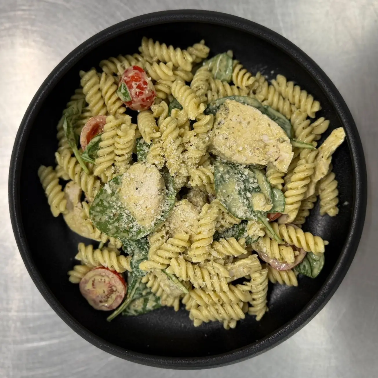 Pesto Pasta with cherry tomatoes, spinach and grated parmesan in a black bowl